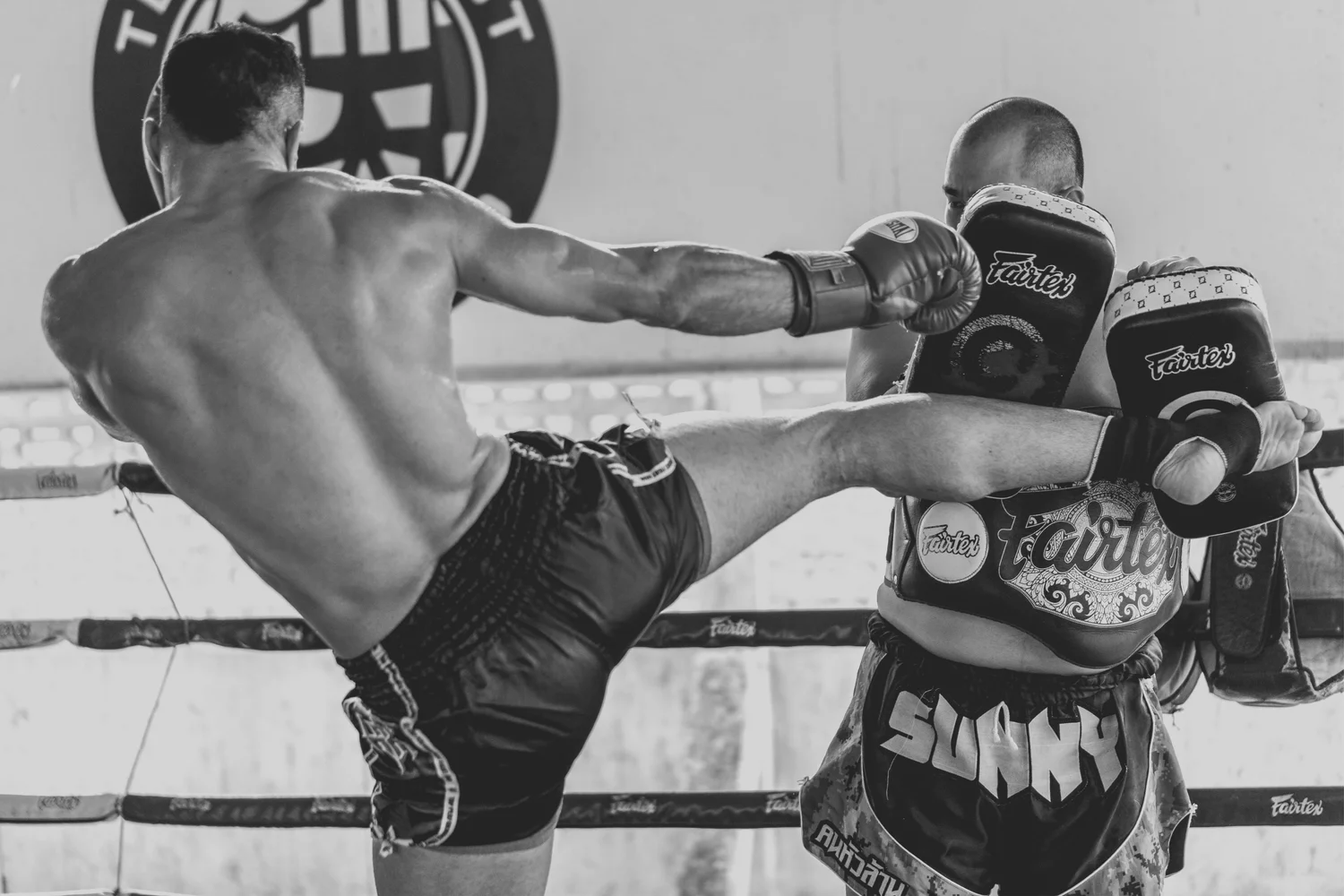 Muay-Thai-Kämpfer führt im Ring einen Seitwärtstritt gegen die Pratzen